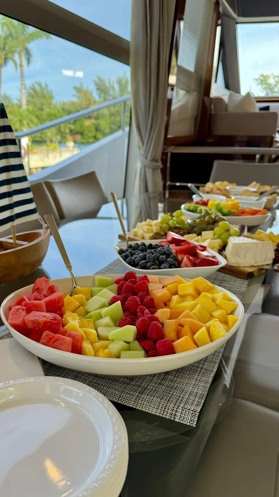 A fruit board of watermelon, melon, mango and raspberries, with the charcuterie laid out behind it